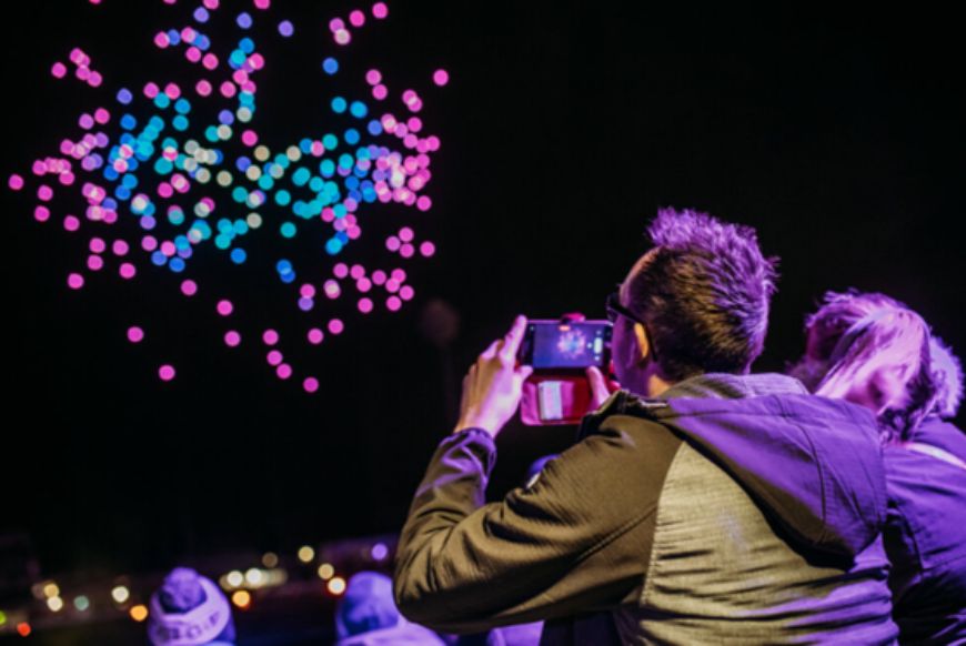 people watching and videoing a drone show